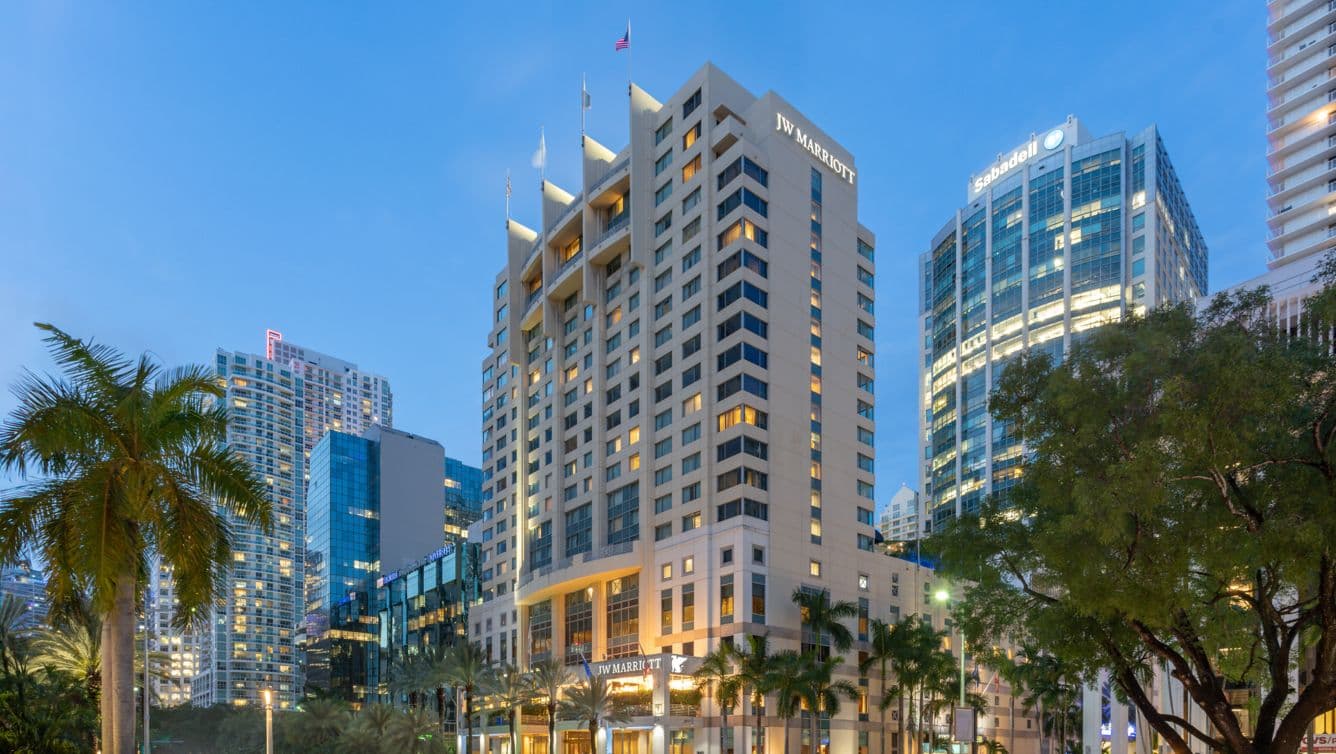 The JW Marriott Miami glass tower rising above Brickell Avenue, set back behind mature palms.
